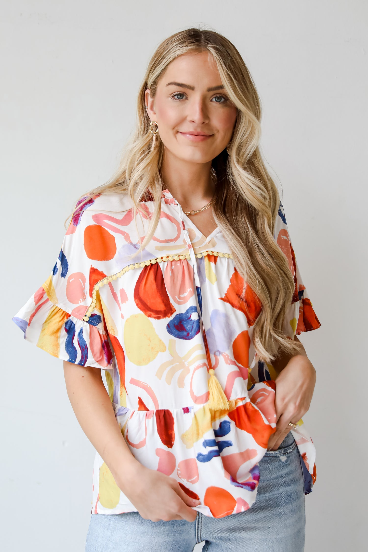 Breezy Sophistication Ivory Ruffle Blouse. Ivory base with blue and orange prints. Yellow tassel