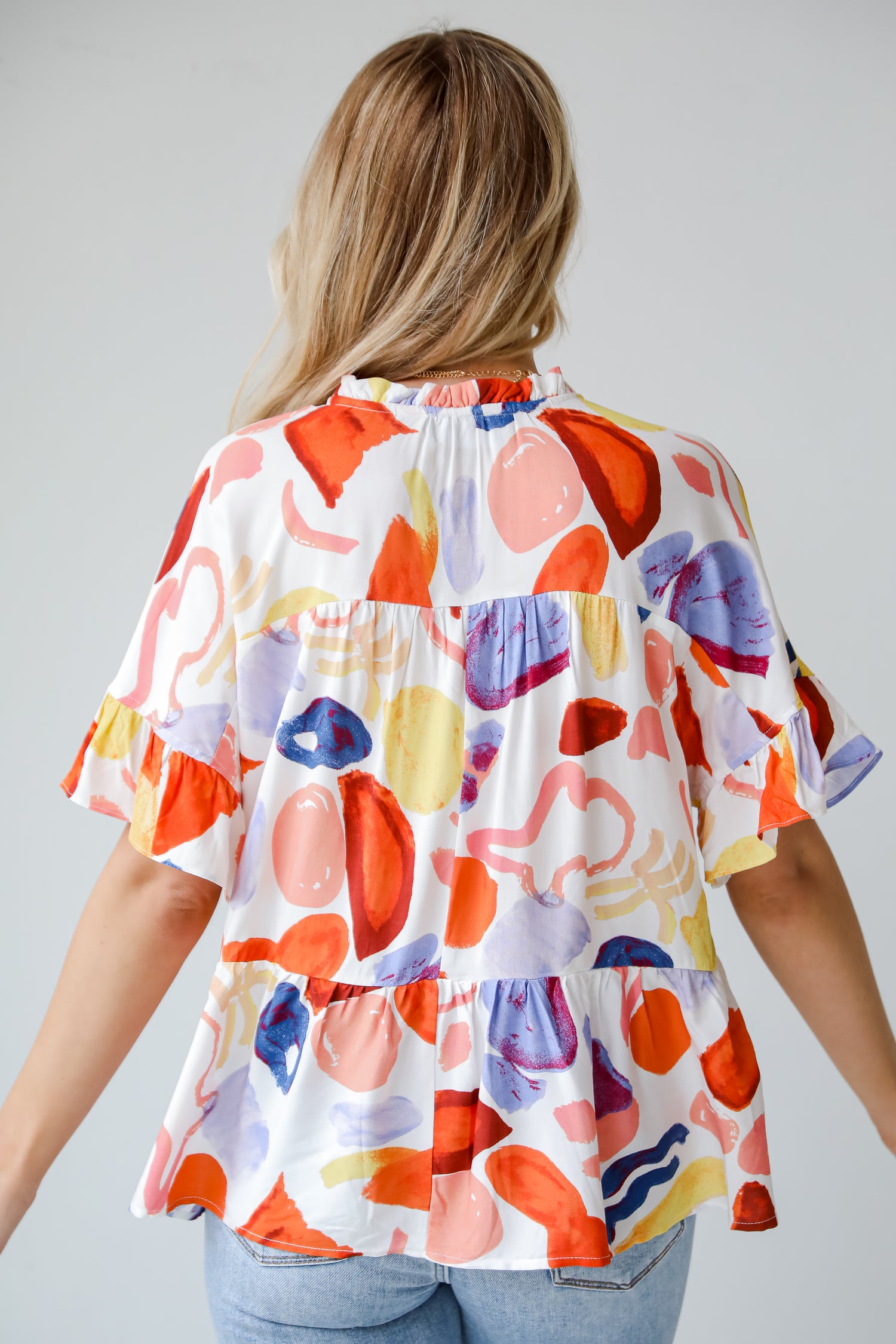 Breezy Sophistication Ivory Ruffle Blouse. Ivory base with blue and orange prints. Yellow tassel